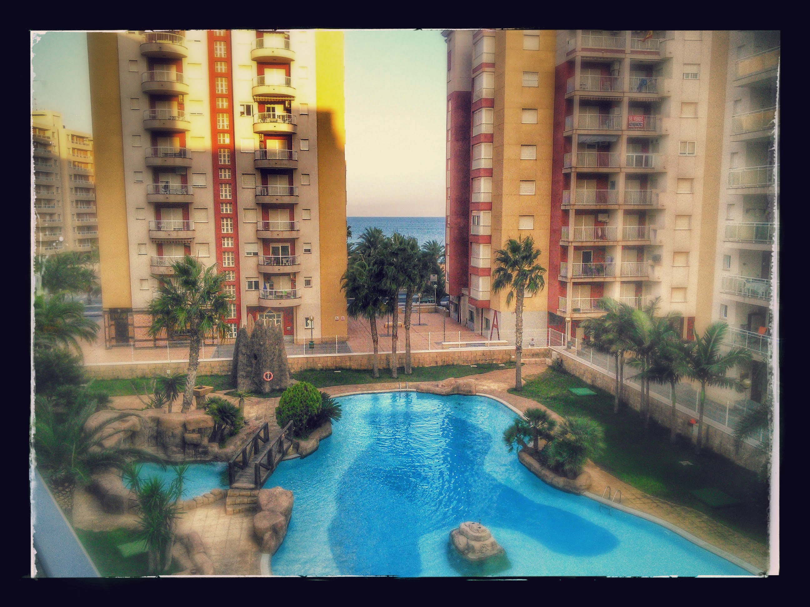 A view from the balcony of a swimming pool, with the ocean in the background